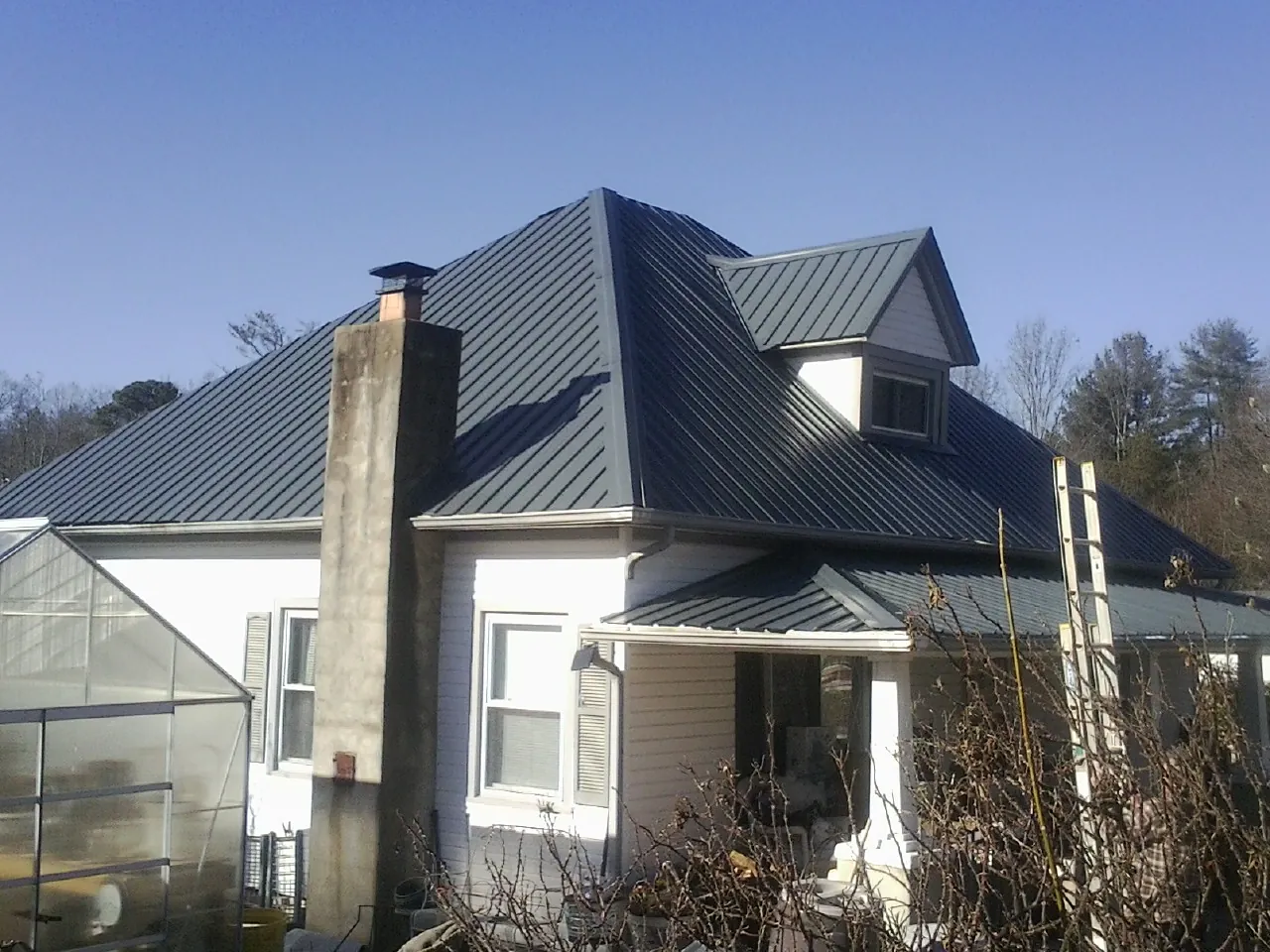 Dark blue standing seam metal roof on a white farmhouse with dormer — Slate & Tile Roof Repair by Roofing Brothers in Anna Maria