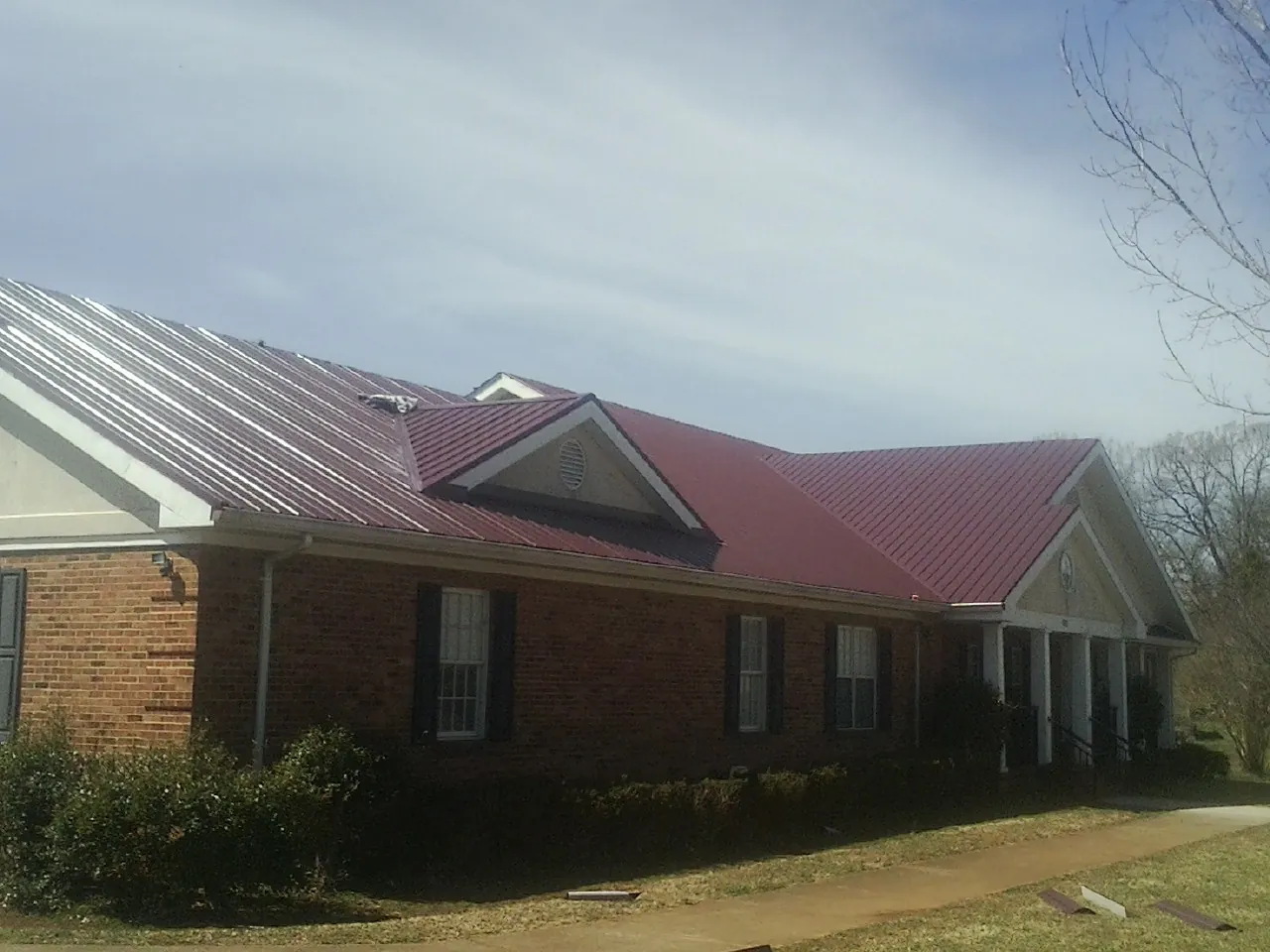 Red metal roof with gabled entries on a long brick building, from a Hail Damage Roof Repair job in Anna Maria