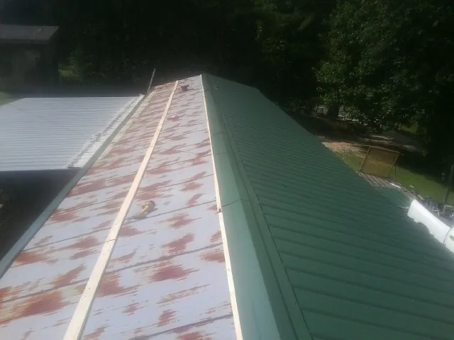 Old rusted panels beside newly installed green metal roofing — Wind Damage Roof Repair by Roofing Brothers in Anna Maria
