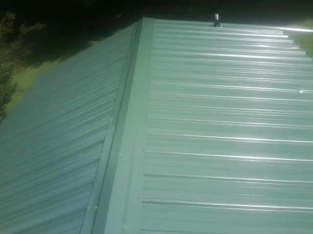New green metal panels meeting at the ridge of a roof — Flat Roof Repair work by our crew in Anna Maria