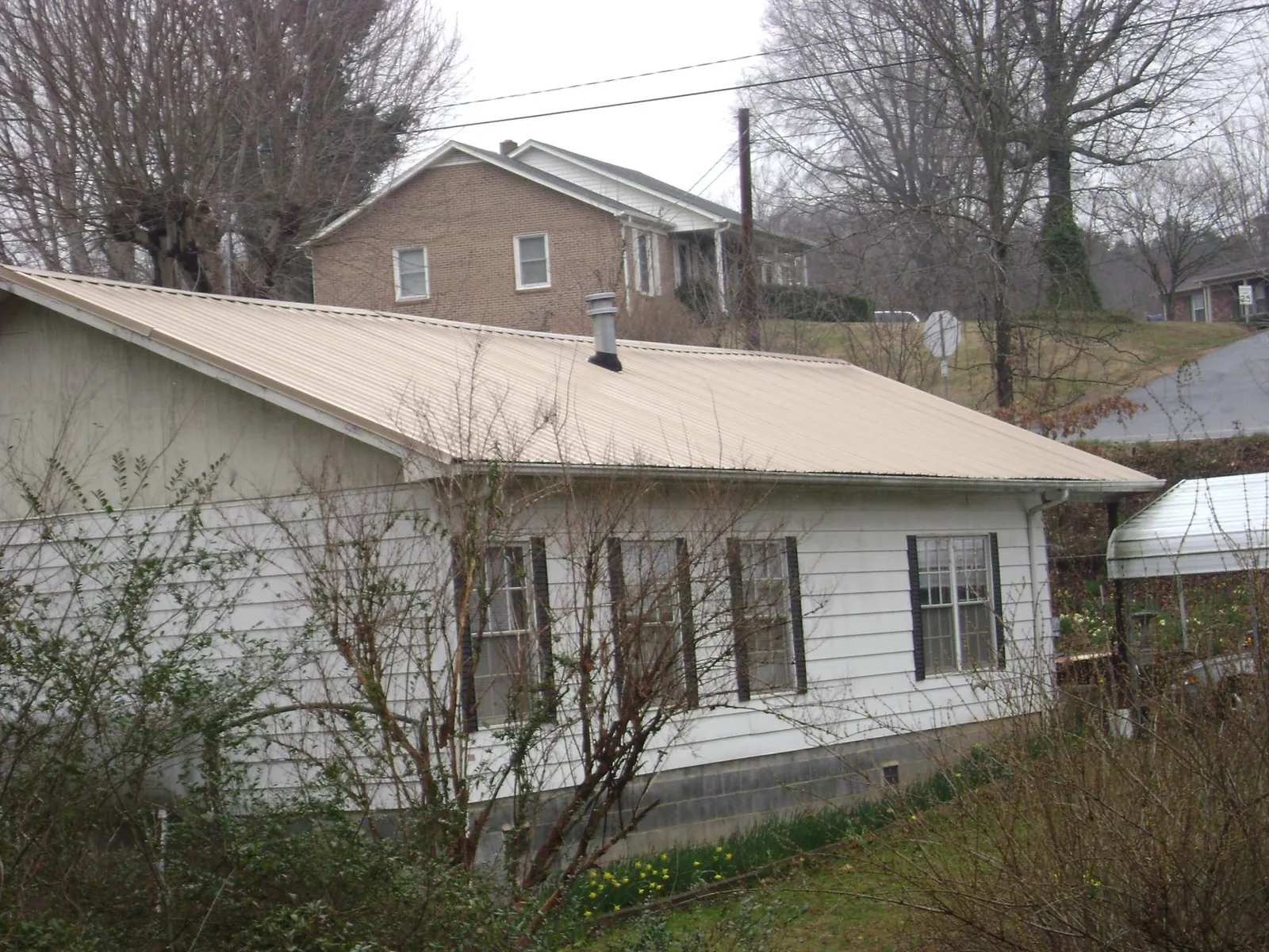 Tan metal roof on a white sided house set into a hillside — Commercial Roofing by Roofing Brothers in Anna Maria